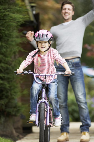 Little Girl in a Helmet Riding a Bike While Dad Cheers Her On